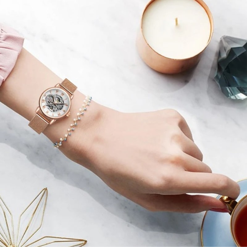Montre Automatique Femme Bracelet Acier Maille & Cadran Ajouré en rose portée sur un poignet de femme qui tient une tasse de café