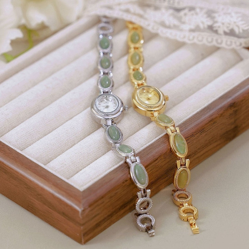Montre Vintage Ovale pour Femme, modèles doré et argenté posés sur un coffret, bracelets ornés de maillons ovales verts, design élégant et raffiné