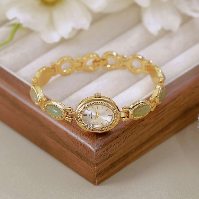 Montre Vintage Ovale pour Femme, boîtier doré avec cadran clair, bracelet doré orné de maillons verts, présentée sur un coffret, style raffiné et féminin