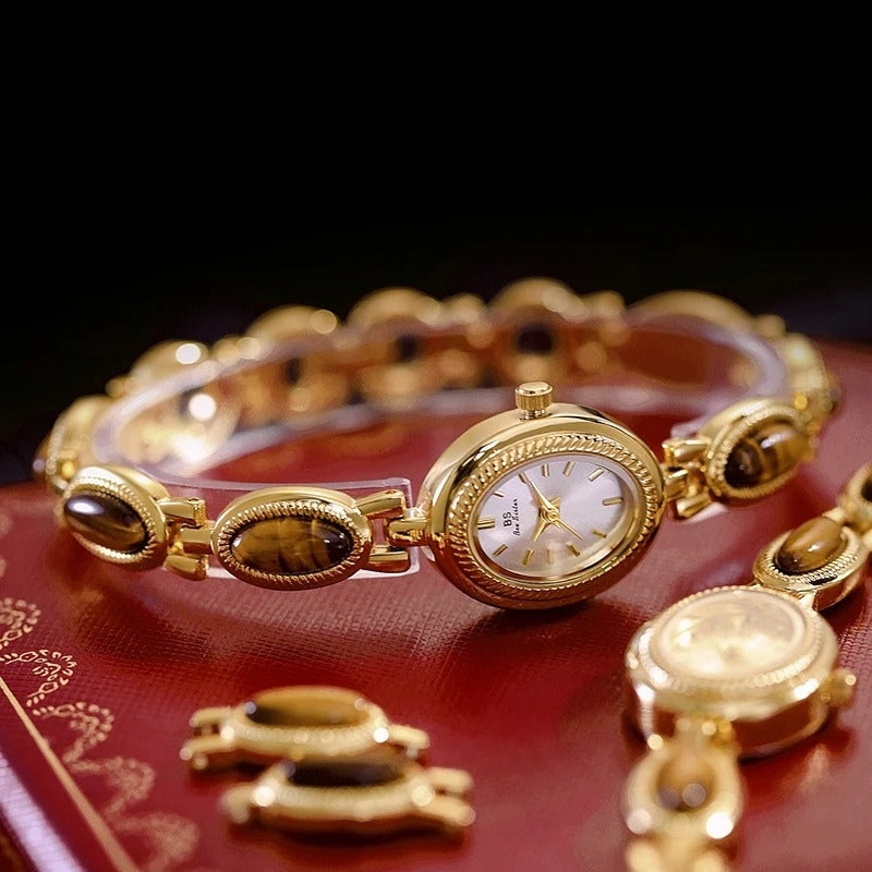 Montre Vintage Ovale pour Femme, boîtier doré avec cadran clair, bracelet orné de maillons ovales dorés et marron, posée sur un coffret rouge, style luxueux et intemporel