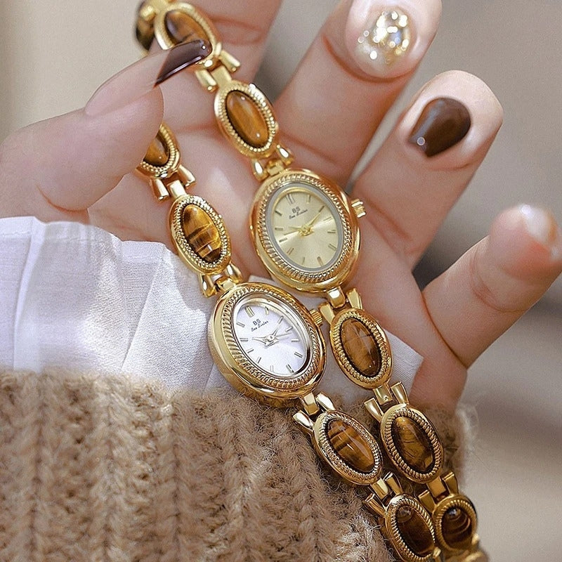 Montre Vintage Ovale pour Femme, boîtier doré avec cadran clair et marron, bracelets ornés de maillons ovales dorés et bruns, portées à la main, style élégant et raffiné. Image