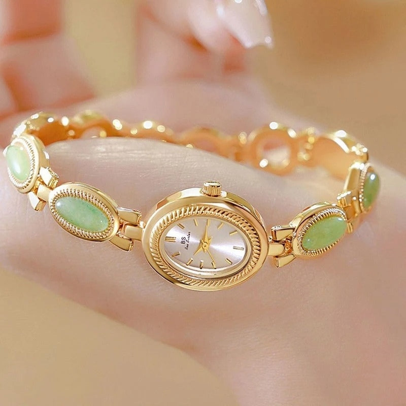 Montre Vintage Ovale pour Femme, boîtier doré avec cadran clair, bracelet doré orné de maillons verts, tenue en main, design élégant et intemporel. Image