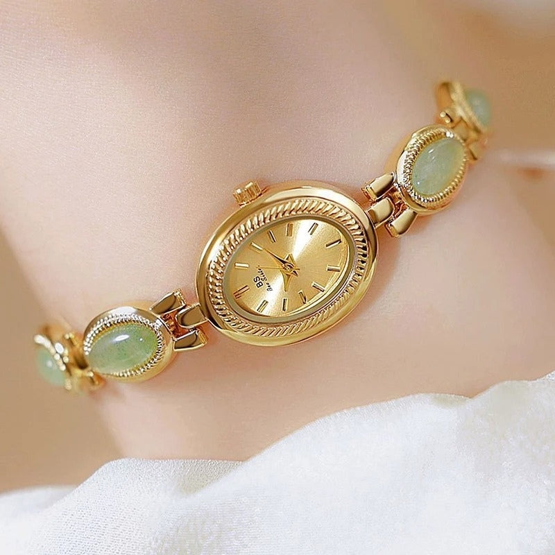 Montre Vintage Ovale pour Femme, boîtier doré avec cadran doré, bracelet doré orné de maillons verts, portée au poignet, style raffiné et féminin.