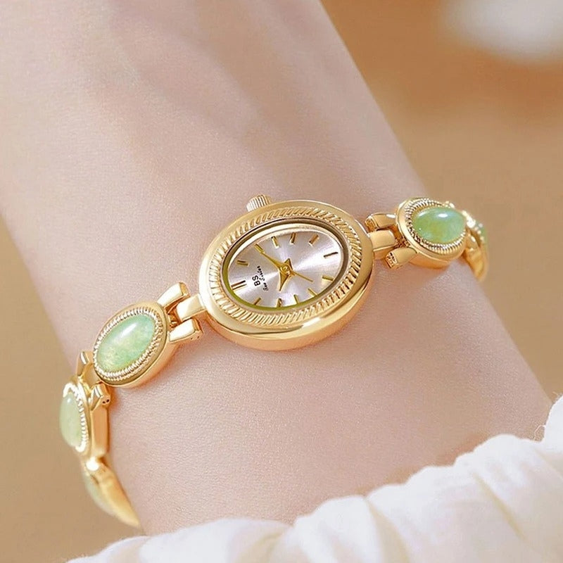 Montre Vintage Ovale pour Femme, boîtier doré avec cadran argenté, bracelet doré orné de maillons verts, portée au poignet, design élégant et intemporel.