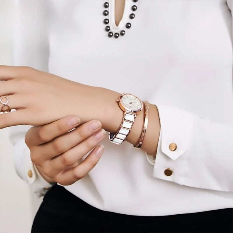 Montre Vintage pour Femme de forme ronde or rose et blanche portée au poignet, assortie de bracelets dorés pour un look chic.