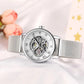 Montre Automatique Femme Bracelet Acier Maille & Cadran Ajouré en argenté couchée sur une table avec des fleurs en arrière plan